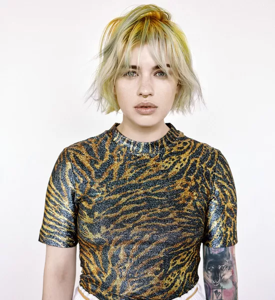 Nikol Hlaváčková je tvůrkyní tohoto účesu. Žena má délku vlasů kratší než po ramena blond v kombinaci se zelenou barnou.